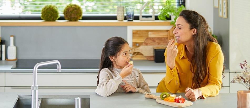 Een vrouw en een kind zitten aan de keukentafel en eten samen.